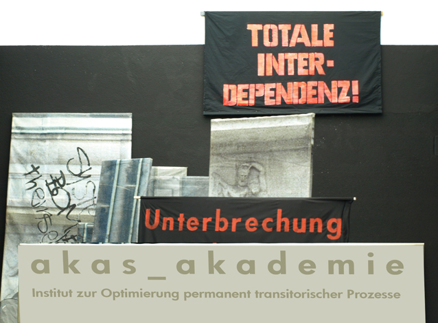 Ausstellungsaufbau mit Schriftflächen „TOTALE INTERDEPENDENZ!“, „Unterbrechung“ und „akas_akademie“.