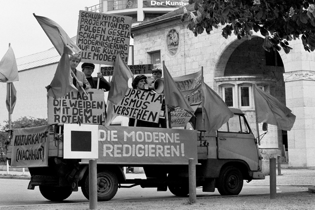Schwarz-weiße Aufnahme von Menschen mit Fahnen und Schriftplakaten auf einem kleinen Lastwagen.