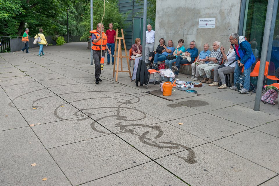 Gruppe bei einer Veranstaltung im Freien; auf dem Boden liegt eine große Seilzeichnung.