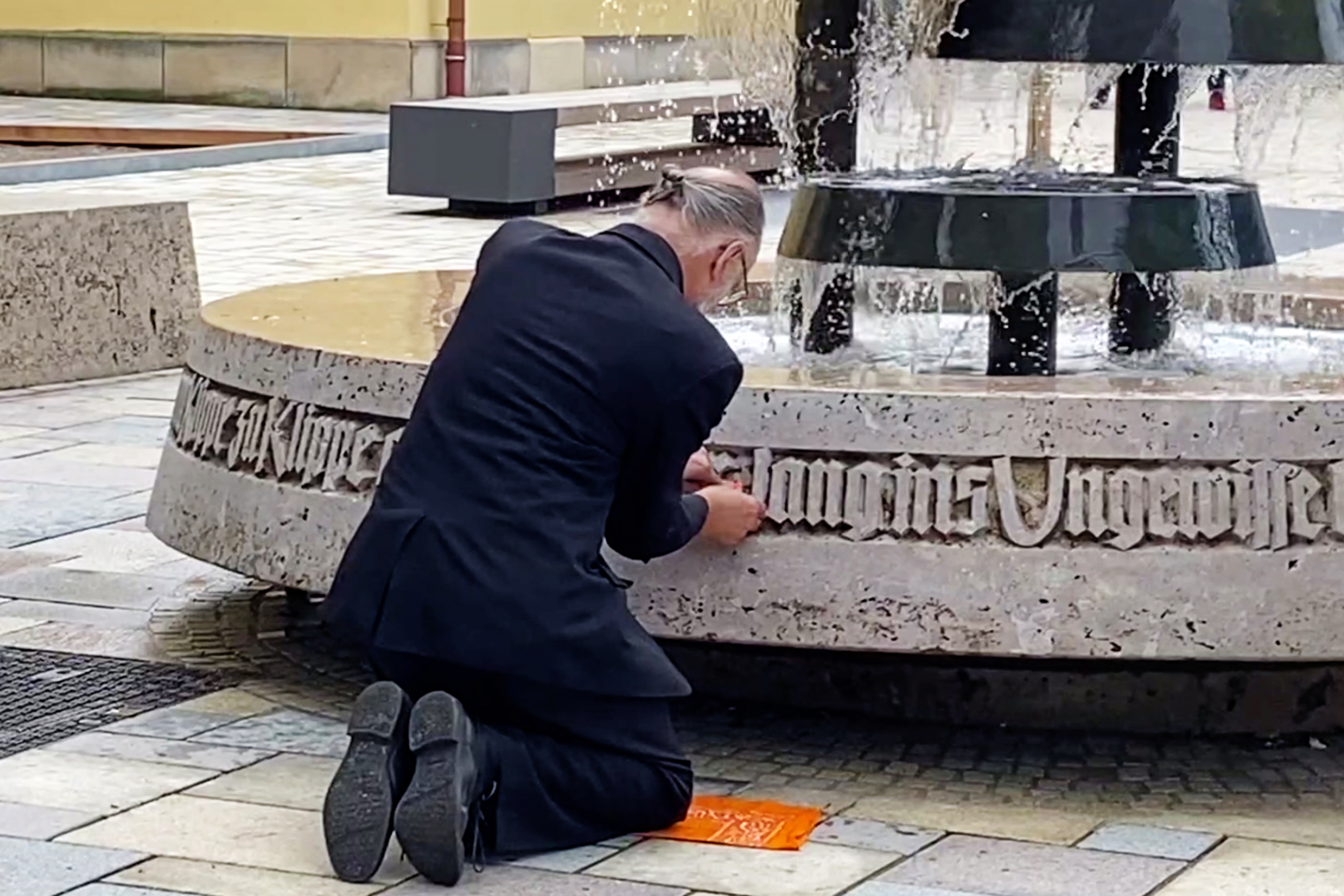 Person kniet am Rand eines Brunnens und arbeitet an einem umlaufenden Schriftband.
