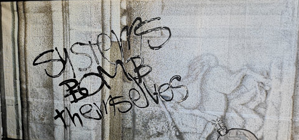 Schwarzer Schriftzug „SYSTEMS BOMB themselves“ aus kurzen Streifen auf einem Figurenrelief.