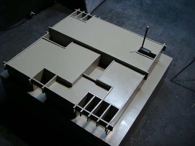 Draufsicht auf ein helles Architekturmodell mit mehreren rechteckigen Räumen und Öffnungen.