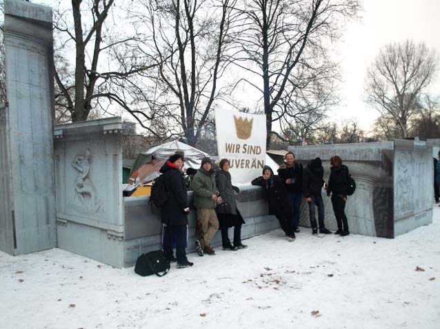 Menschen stehen vor der Installation und einem Schild „WIR SIND UNBEUGSAM“ im Schnee.