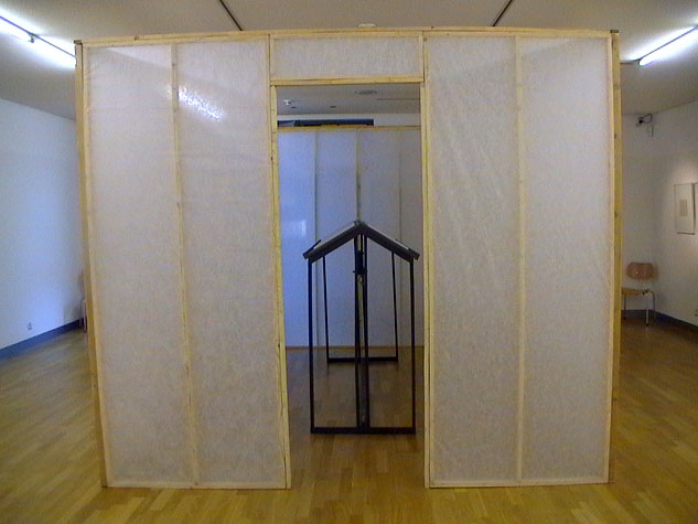 Frontansicht der transparenten Wandkonstruktion mit einem schmalen hausförmigen Rahmen im Eingang.