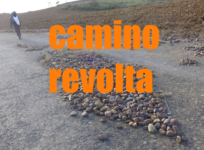 Fotografie eines Weges mit verstreuten Steinen und einer gehenden Person; darüber steht orange „camino revolta“.