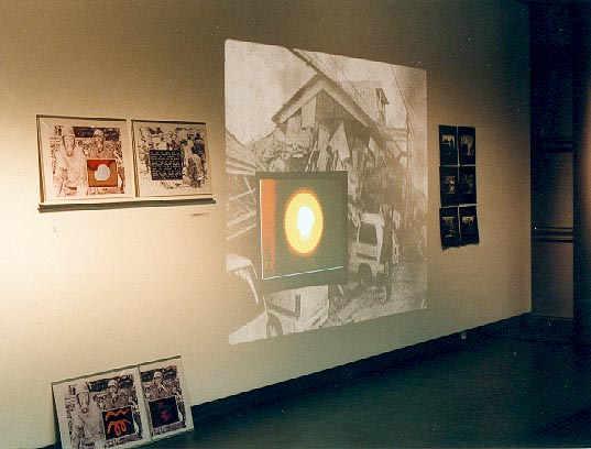 Wandinstallation mit historischen Bildern und einer leuchtenden runden Farbform auf einer Bildfläche.