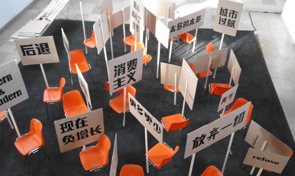 Orangefarbene Stühle zwischen zahlreichen Tafeln mit chinesischen Schriftzeichen in einem Ausstellungsraum.