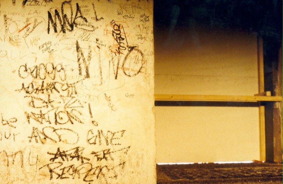 Nahaufnahme einer Wand mit handschriftlichen Schriftzügen neben einer gelb beleuchteten Öffnung.