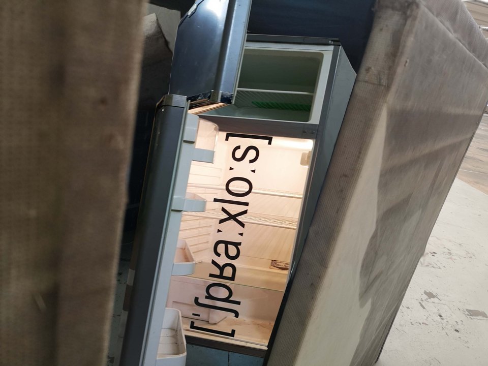 Blick durch einen schmalen Spalt zwischen Wandflächen auf einen Rahmen mit Lautschrift-Zeichen.