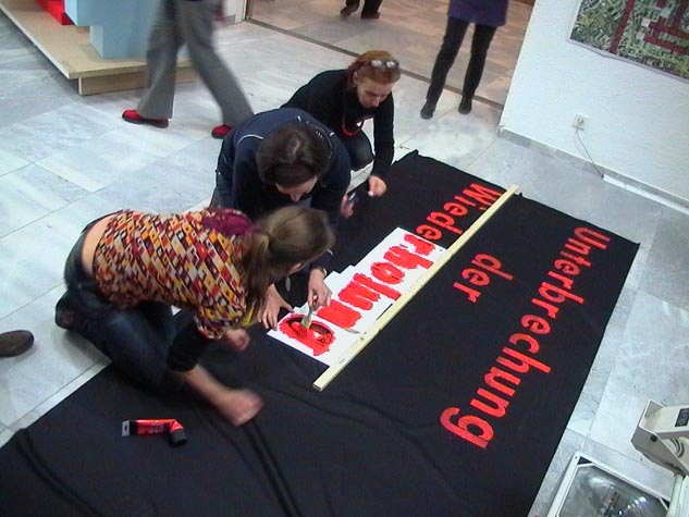 Mehrere Menschen befestigen rote Buchstaben auf einer großen schwarzen Fläche auf dem Boden.