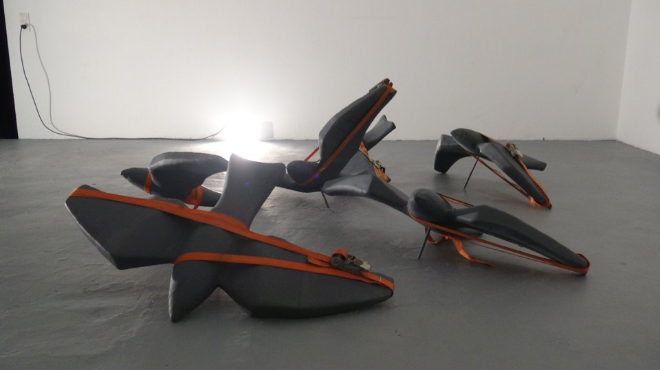 Ansicht mehrerer grauer Sitzformen mit orangefarbenen Gurten in einem hellen Raum.