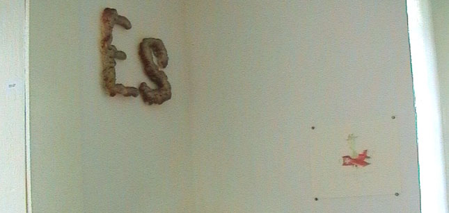 Braune plastische Buchstaben bilden das Wort „Es“ an einer hellen Wand.