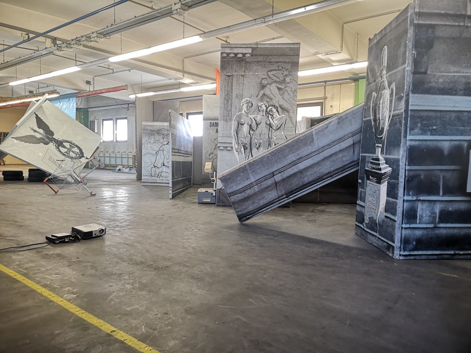 Bedruckte Architekturflächen und Figurenzeichnungen bilden einen Aufbau in einer Ausstellungshalle.