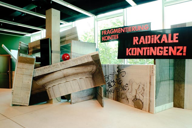 Schräg gestellte Architekturflächen und rote Schriftplakate, darunter „RADIKALE KONTINGENZ!“.