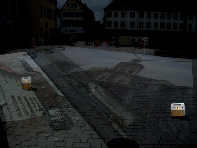 Kleine helle Kisten stehen bei Nacht auf einem gepflasterten Platz mit Straßenbahnschienen.