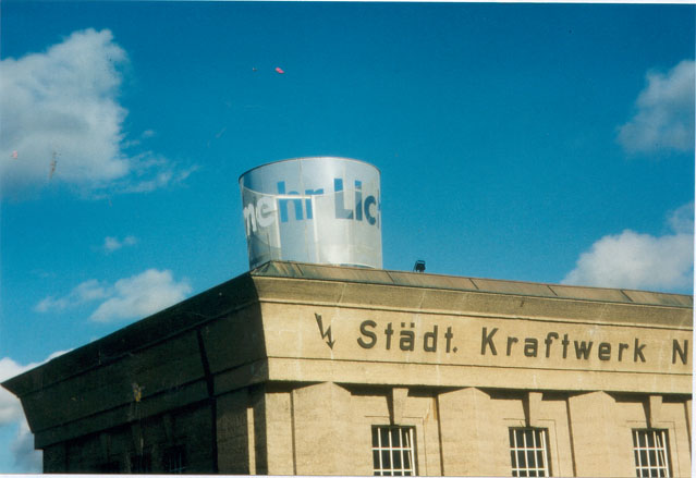 Blick auf den Schriftzylinder und das Gebäudedach vor blauem Himmel.