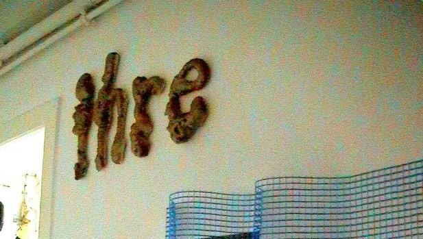Das Wort „ihre“ aus braunen plastischen Buchstaben an einer Wand über einem Gitter.