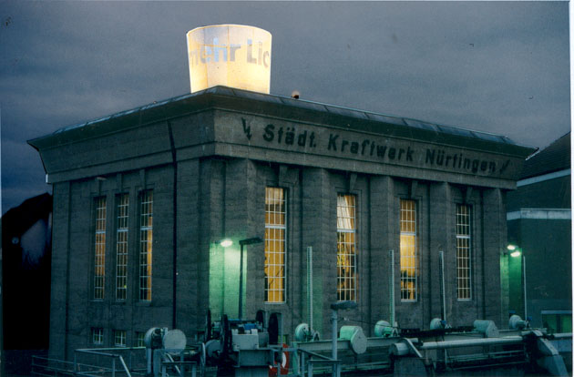 Beleuchteter Schriftzylinder auf dem Dach eines Gebäudes mit der Fassadenaufschrift „Städt. Kraftwerk Nürtingen“.
