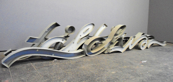 Helle geschwungene Buchstaben des Schriftzugs „Liebherr“ liegen auf einem Boden.