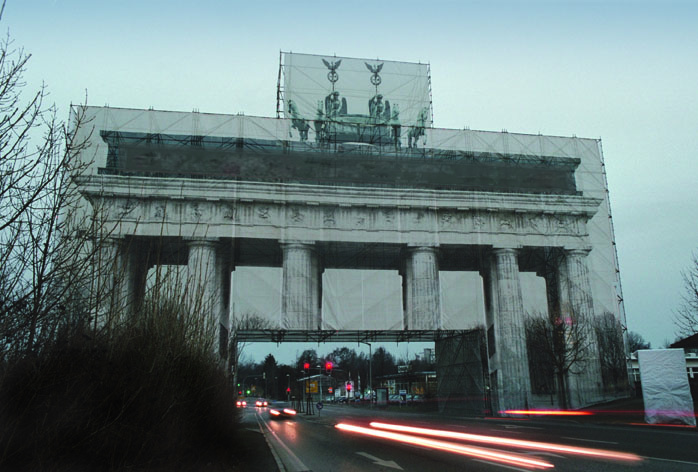 Ansicht eines großen Tores bei Dämmerung mit einer bedruckten Verkleidung; davor verlaufen Lichtspuren des Verkehrs.