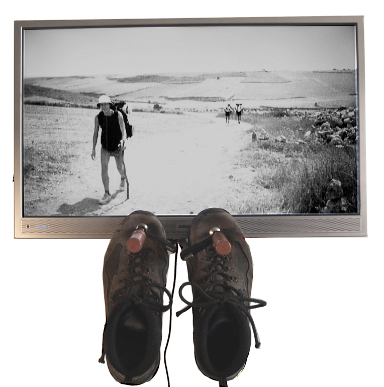 Gerahmte Schwarz-Weiß-Fotografie einer gehenden Person; darunter hängt ein Paar Schuhe.