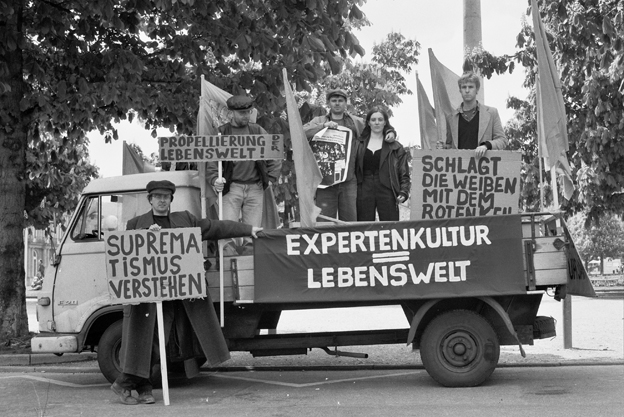 Kleiner Lastwagen mit Menschen und Fahnen; am Fahrzeug steht „EXPERTENKULTUR LEBENSWELT“.