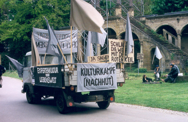 Kleiner Lastwagen mit Fahnen und Schriftplakaten steht an einem Parkweg.