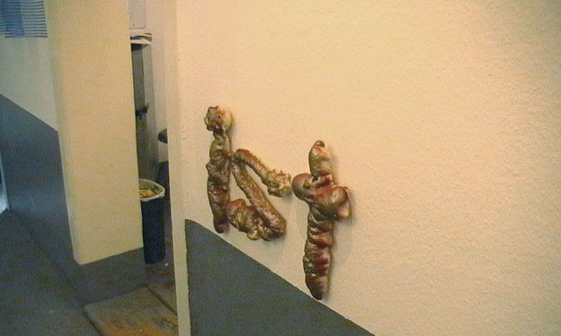 Braune plastische Buchstaben bilden das Wort „ist“ an einer Wand neben einem Durchgang.