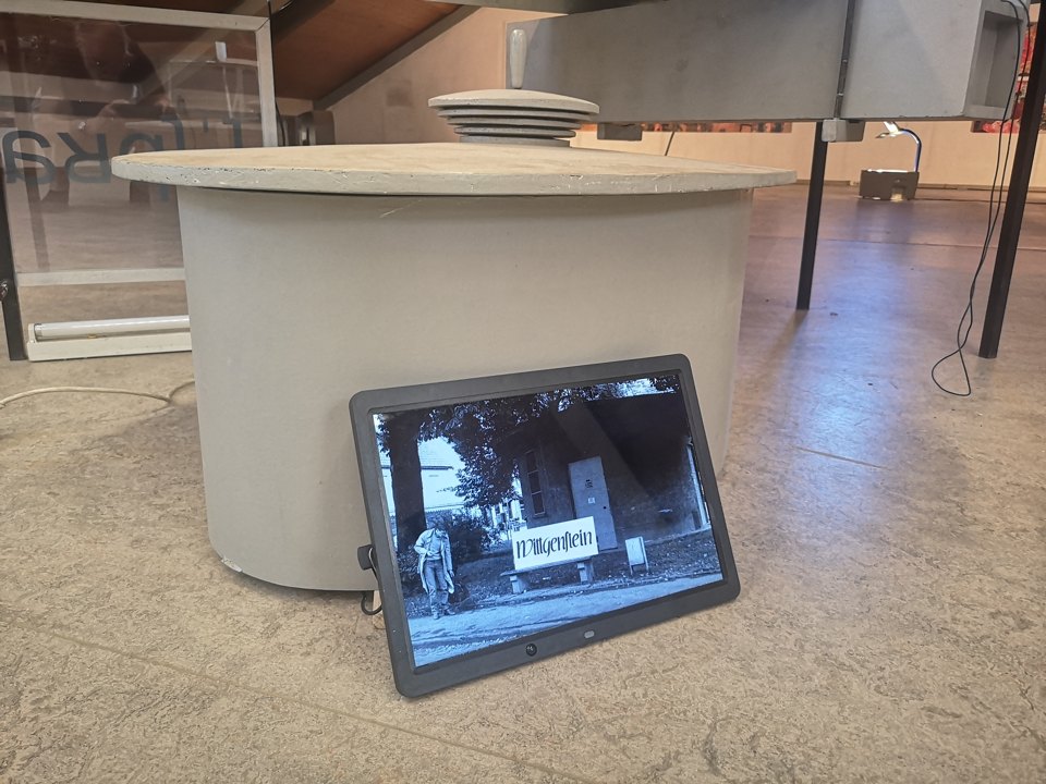 Kleine Bildschirmansicht steht vor einer weißen runden Tischform; auf dem Tisch liegen gestapelte Teller.