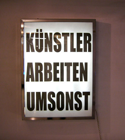 Leuchtkasten mit der Aufschrift „KÜNSTLER ARBEITEN UMSONST“.