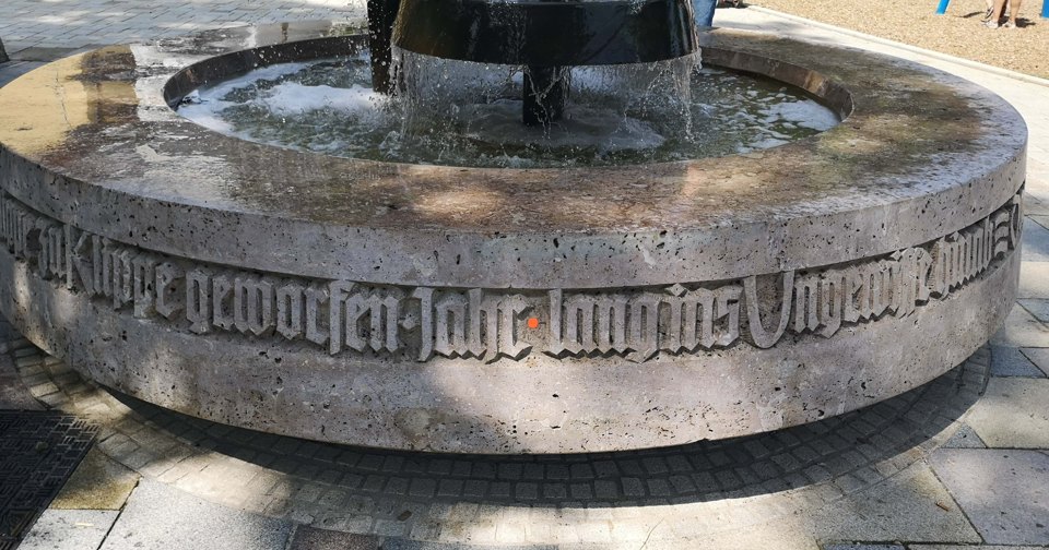 Nahaufnahme des Brunnens mit Wasser und einem Schriftband um den steinernen Rand.
