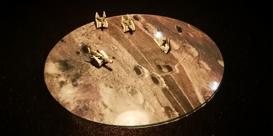 Nahaufnahme einer kreisförmigen Szene mit kleinen Figuren, Kratern und Fußspuren.