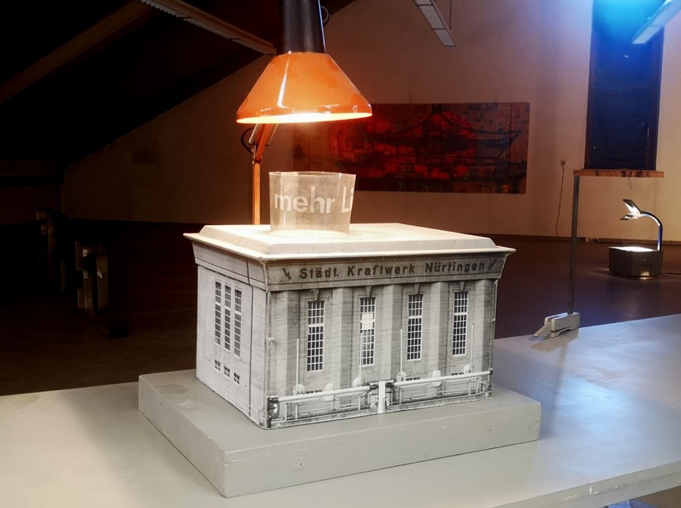 Weißes Gebäudemodell auf einem Tisch unter einer orangefarbenen Lampe.