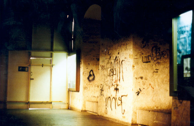 Nächtliche Ansicht einer beschrifteten alten Wand mit einem beleuchteten Durchgang und Bildschirm.