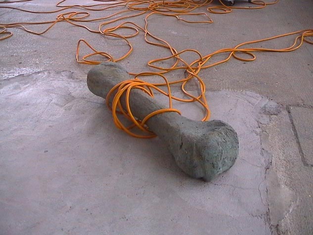 Orangefarbenes Seil ist um einen grauen zylindrischen Gegenstand auf dem Boden gewickelt.
