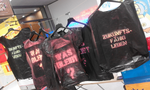 Mehrere dunkle Stofftaschen mit aufgedruckten pinkfarbenen und grünen Schriftzügen.