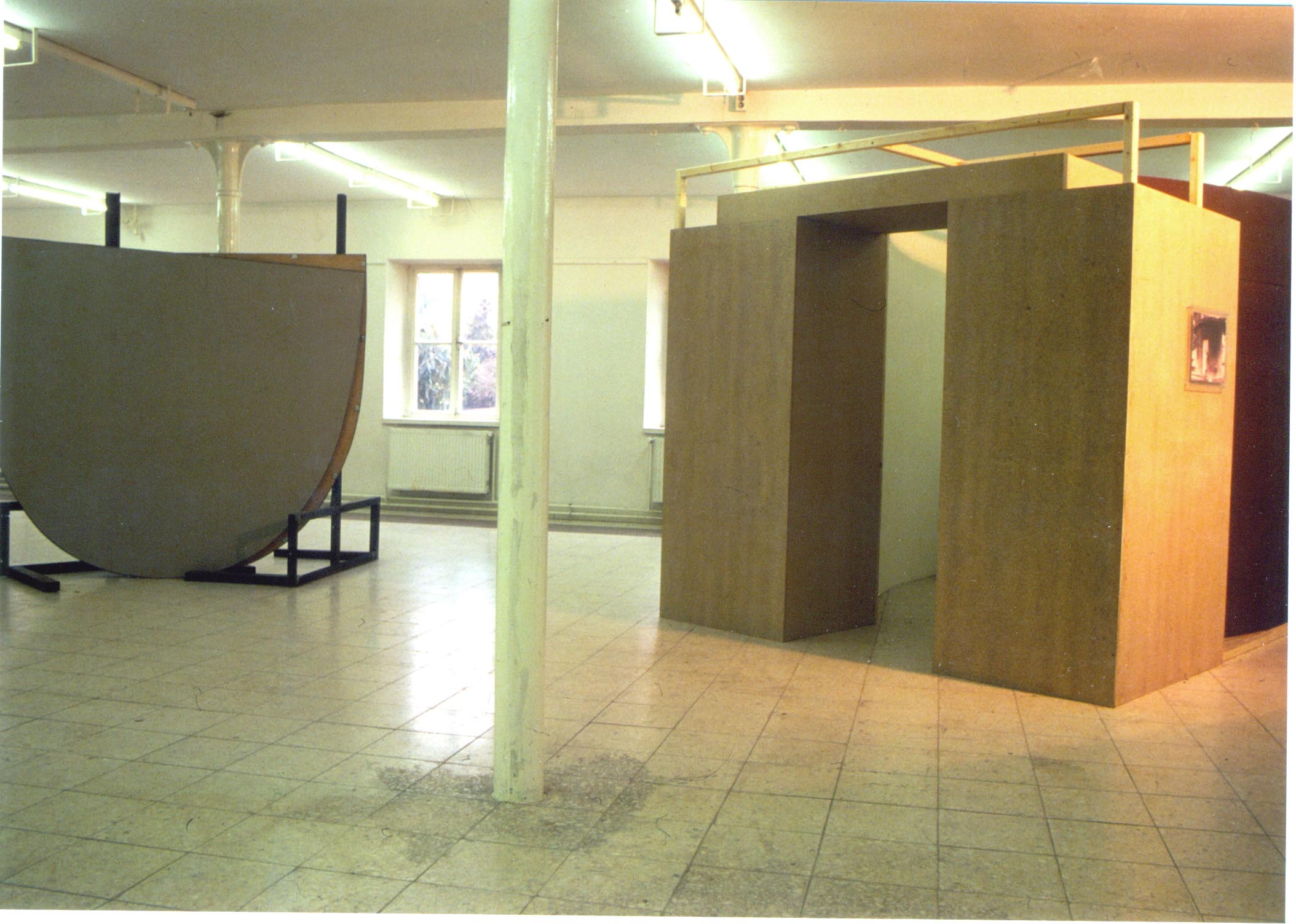 Rauminstallation aus hohen gebogenen und geraden Wandflächen; in der Mitte liegt ein Durchgang.