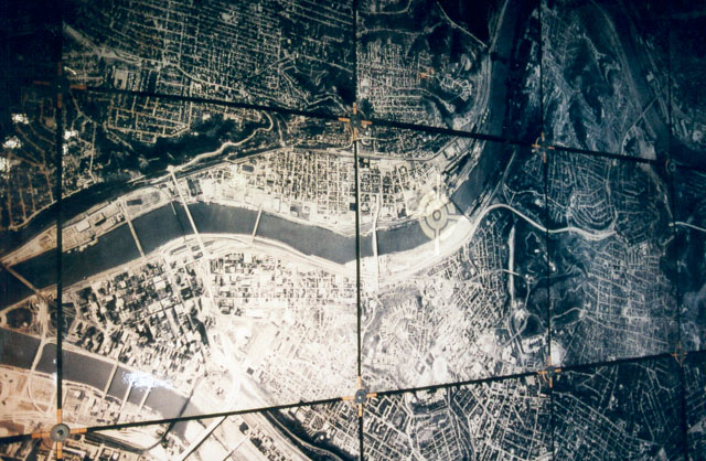 Schwarz-weiße Luftaufnahme einer Stadt und eines Flusses, unterteilt durch gerade Linien.