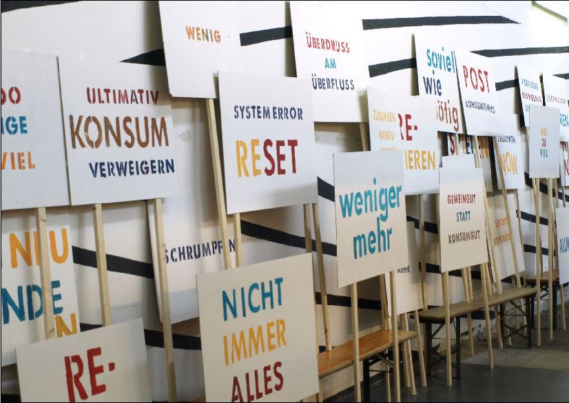 Viele weiße Plakate mit unterschiedlich farbigen Schriftzügen stehen an Stäben dicht nebeneinander.